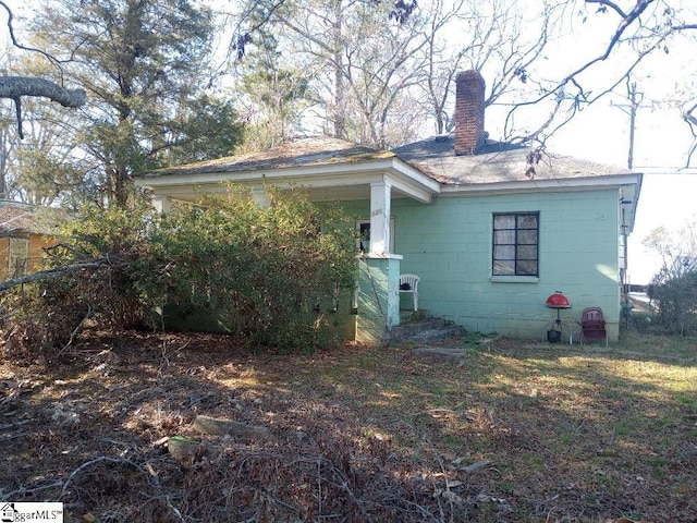 view of home's exterior with a chimney and concrete block siding