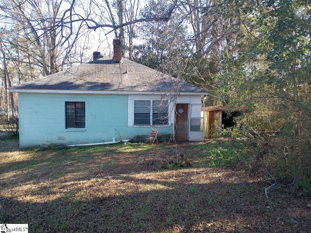 view of front of house featuring a chimney, concrete block siding, and roof with shingles