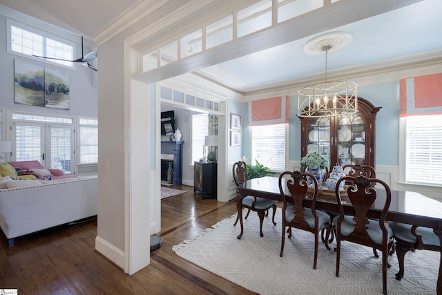 dining area featuring dark wood-style floors, french doors, crown molding, an inviting chandelier, and a glass covered fireplace