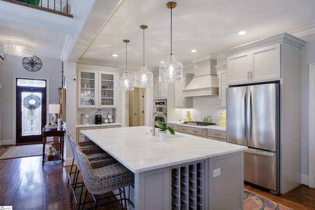 kitchen featuring glass insert cabinets, stainless steel appliances, white cabinetry, a center island with sink, and custom range hood