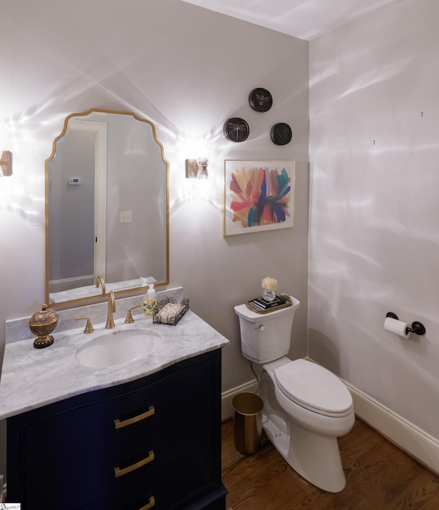 half bathroom featuring wood finished floors, vanity, toilet, and baseboards