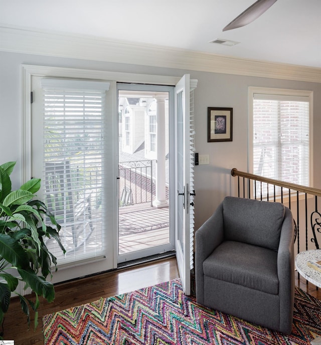 doorway with plenty of natural light, wood finished floors, visible vents, and crown molding