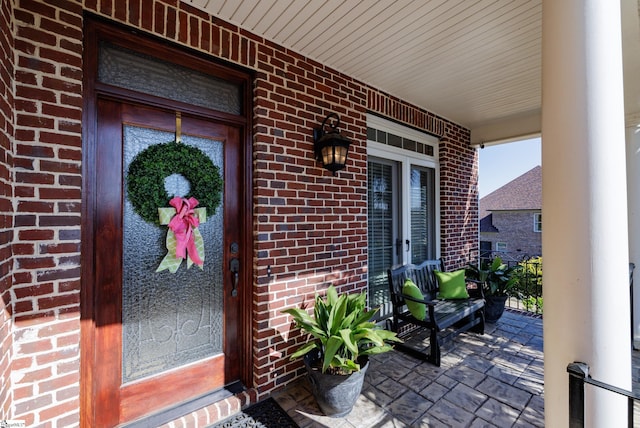 entrance to property featuring covered porch and brick siding