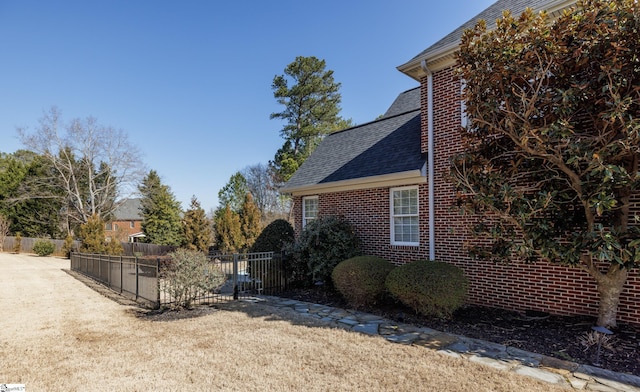 view of home's exterior with roof with shingles, fence, and brick siding