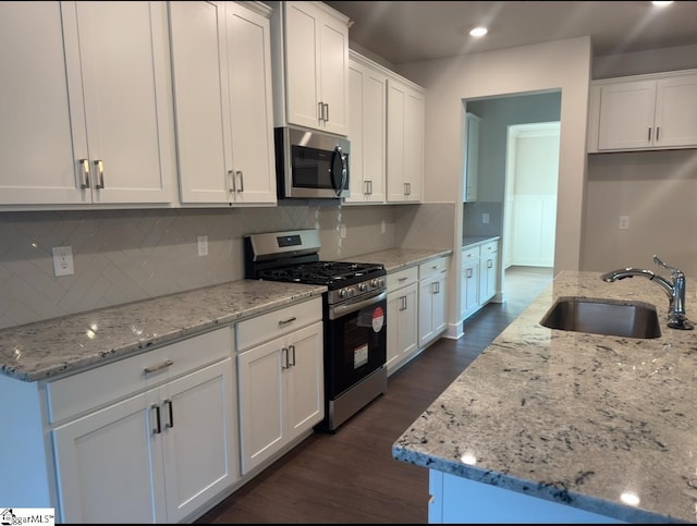 kitchen featuring dark wood finished floors, appliances with stainless steel finishes, light stone countertops, white cabinetry, and a sink