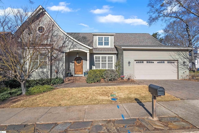 traditional-style house with an attached garage, a shingled roof, decorative driveway, and a front yard