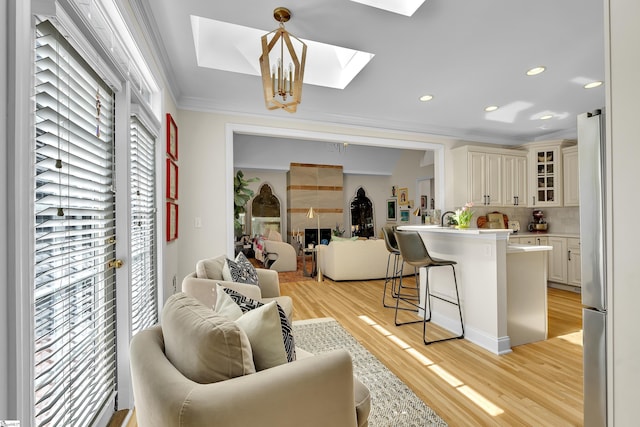 living area with ornamental molding, a skylight, light wood finished floors, and recessed lighting