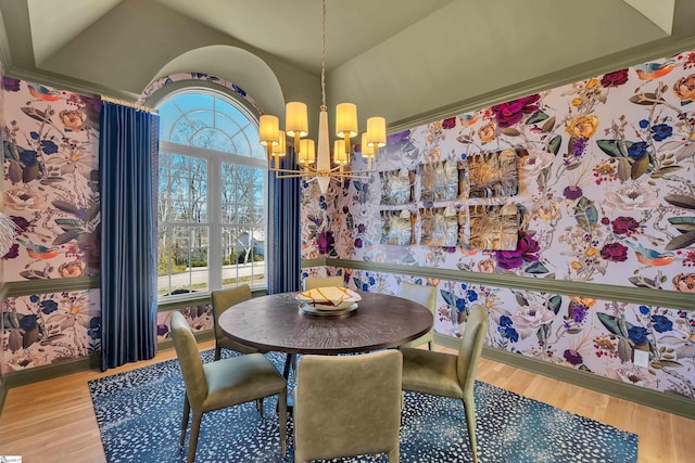 dining room featuring lofted ceiling, wallpapered walls, wood finished floors, and an inviting chandelier