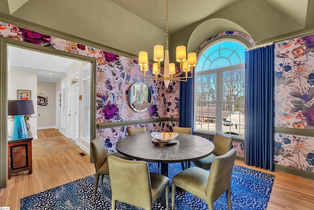 dining area with a chandelier, lofted ceiling, wood finished floors, baseboards, and wallpapered walls