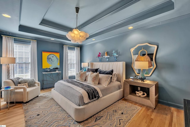 bedroom with baseboards, wood finished floors, a raised ceiling, and crown molding