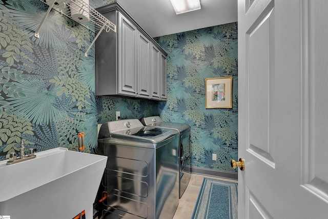 washroom with separate washer and dryer, a sink, baseboards, cabinet space, and wallpapered walls