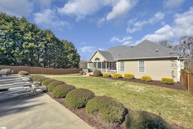 back of property with a shingled roof, a sunroom, a fenced backyard, a yard, and a patio area