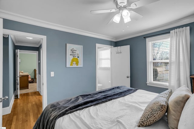 bedroom featuring crown molding, a ceiling fan, ensuite bath, wood finished floors, and baseboards