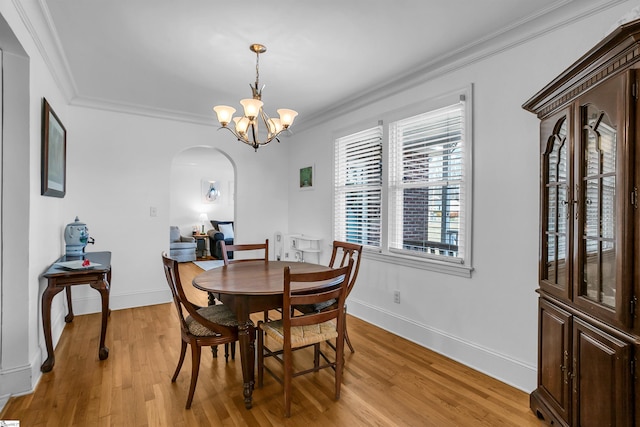 dining area featuring light wood finished floors, arched walkways, a chandelier, and crown molding