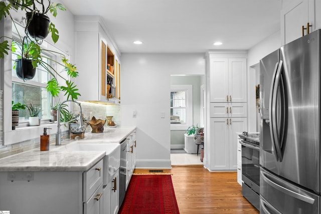 kitchen with light stone counters, stainless steel appliances, white cabinets, light wood finished floors, and tasteful backsplash