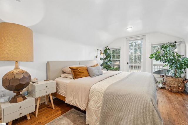 bedroom with lofted ceiling, access to exterior, and wood finished floors