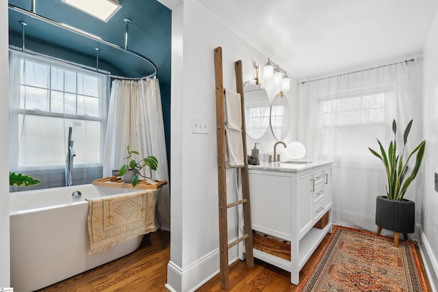 bathroom featuring a soaking tub, vanity, baseboards, and wood finished floors