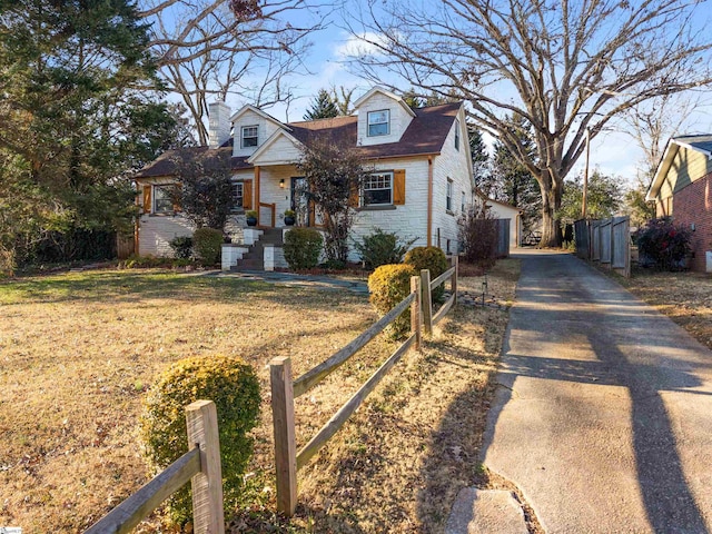 cape cod-style house featuring a chimney, fence, driveway, and a front lawn