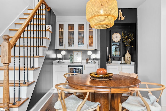 dining area featuring dark wood-style flooring, a dry bar, stairway, beverage cooler, and baseboards