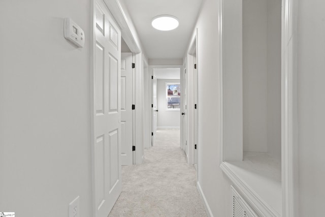 corridor featuring light colored carpet and baseboards