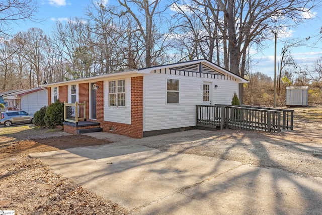 view of front facade with crawl space, brick siding, a wooden deck, and concrete driveway