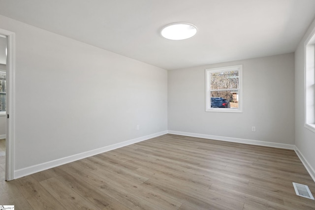 empty room with baseboards, visible vents, and light wood finished floors