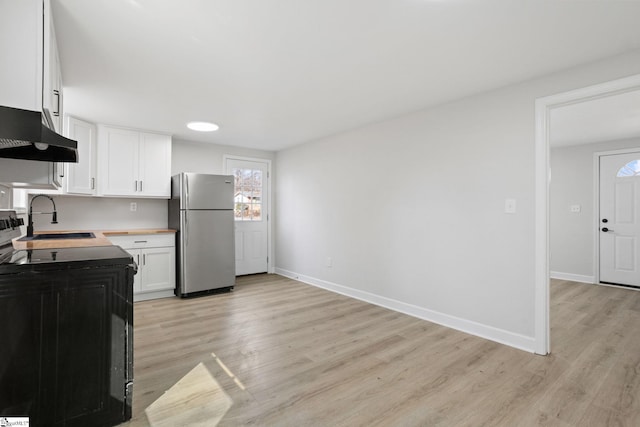 kitchen with black range with electric cooktop, light wood-style flooring, a sink, white cabinets, and freestanding refrigerator