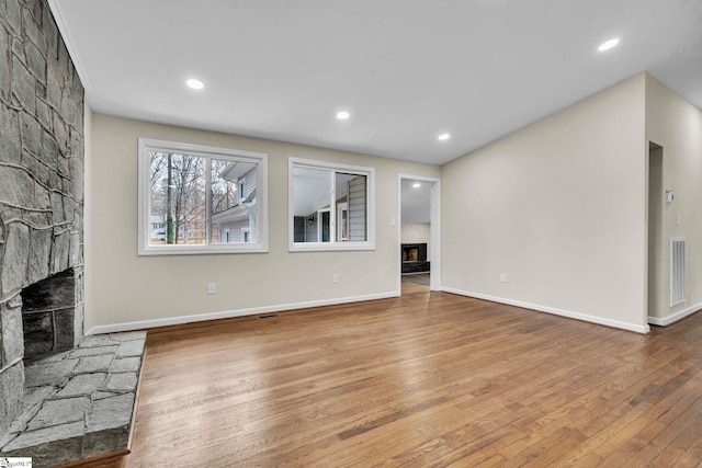 unfurnished living room featuring a fireplace with raised hearth, recessed lighting, wood finished floors, and baseboards