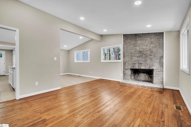 unfurnished living room with baseboards, a stone fireplace, visible vents, and light wood-style floors