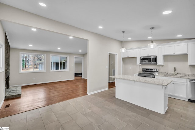 kitchen featuring a kitchen island, appliances with stainless steel finishes, decorative light fixtures, light stone countertops, and white cabinetry