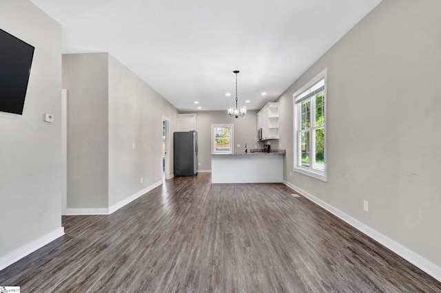 unfurnished living room with dark wood finished floors, baseboards, and an inviting chandelier