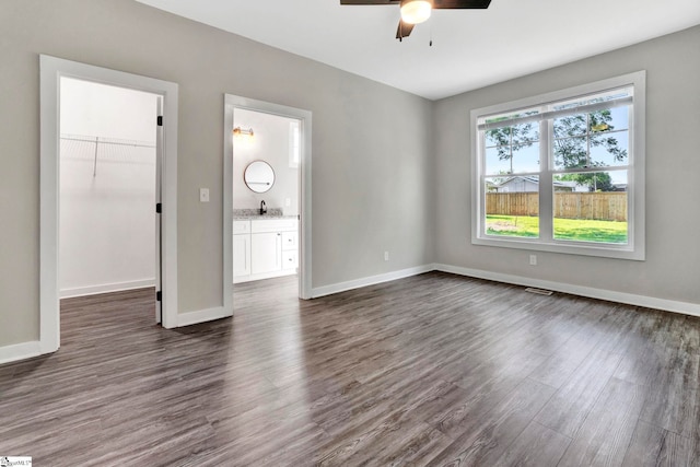 unfurnished bedroom featuring dark wood-style floors, a spacious closet, baseboards, and a closet