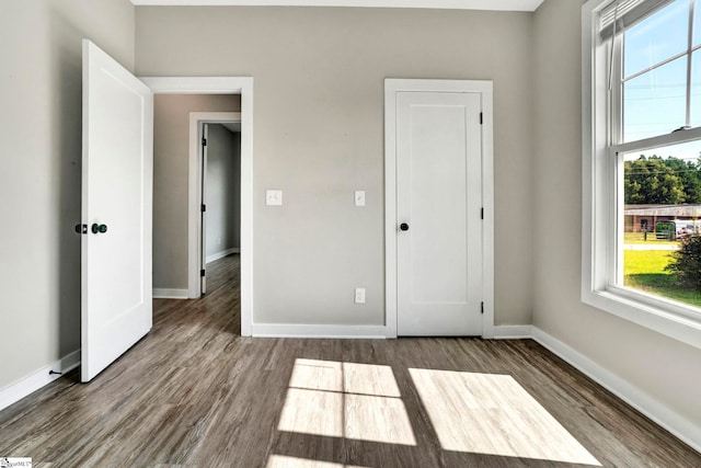 unfurnished bedroom featuring multiple windows, baseboards, and dark wood finished floors