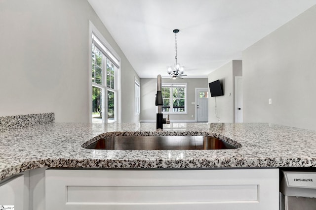 kitchen with light stone counters, pendant lighting, an inviting chandelier, white cabinetry, and a sink