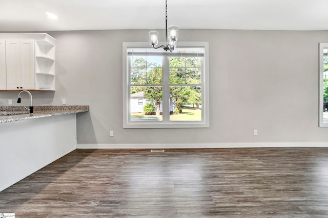 unfurnished dining area with dark wood-style floors, an inviting chandelier, a sink, and baseboards