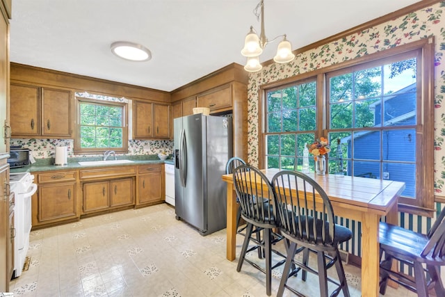 kitchen with brown cabinets, decorative light fixtures, an inviting chandelier, a sink, and white appliances