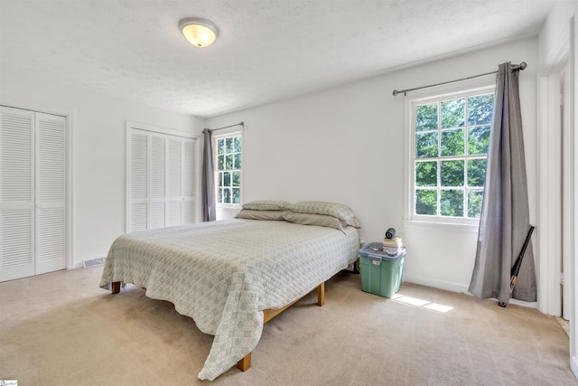 bedroom featuring light carpet, a textured ceiling, baseboards, and multiple closets