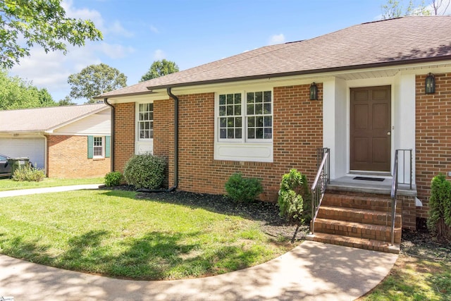 view of front facade with entry steps, a shingled roof, a front lawn, and brick siding