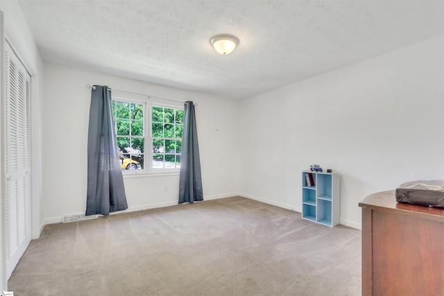 interior space featuring a textured ceiling, baseboards, visible vents, and light colored carpet