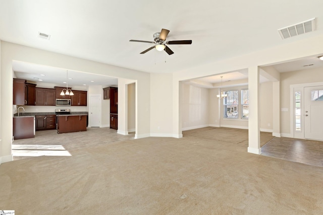 unfurnished living room with light carpet, a sink, visible vents, and baseboards