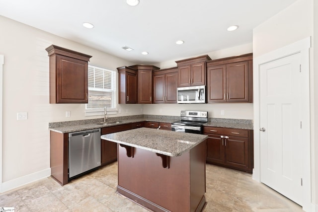 kitchen with a kitchen island, a kitchen breakfast bar, light stone countertops, stainless steel appliances, and a sink