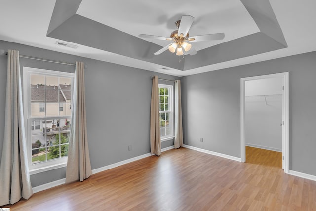 spare room with ceiling fan, light wood finished floors, a raised ceiling, and baseboards