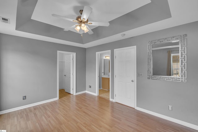 unfurnished bedroom with light wood-type flooring, a raised ceiling, visible vents, and baseboards