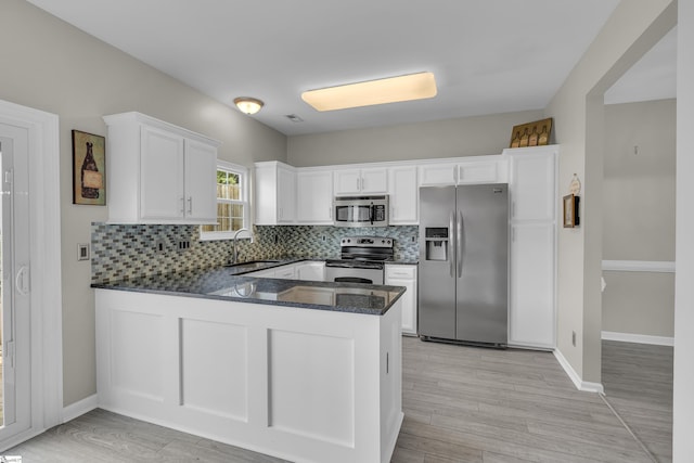 kitchen with tasteful backsplash, white cabinets, appliances with stainless steel finishes, a peninsula, and a sink