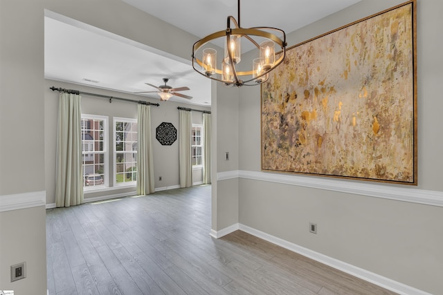 empty room with light wood-type flooring, visible vents, baseboards, and ceiling fan with notable chandelier