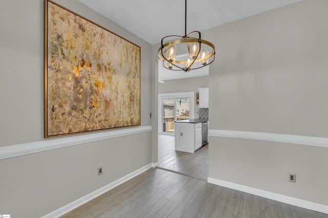 unfurnished dining area featuring light wood-style floors, a chandelier, and baseboards