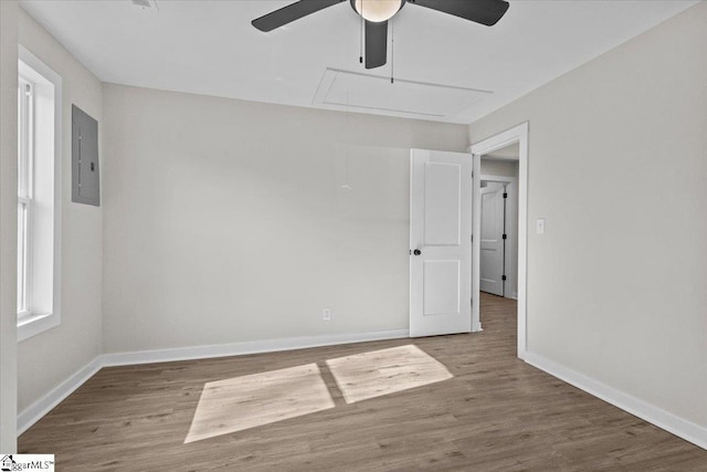 spare room with attic access, electric panel, baseboards, and wood finished floors