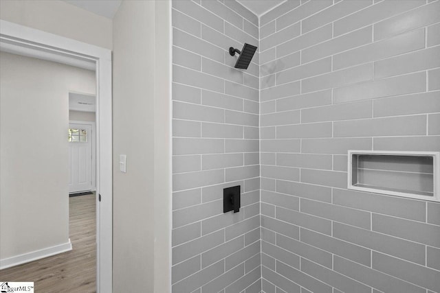 bathroom with baseboards, tiled shower, and wood finished floors