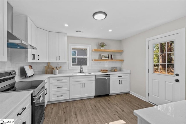 kitchen with wall chimney exhaust hood, appliances with stainless steel finishes, white cabinetry, open shelves, and a sink