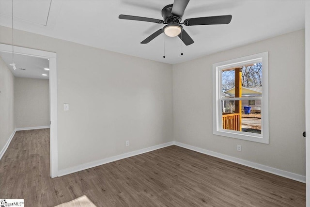 spare room with attic access, baseboards, ceiling fan, and dark wood-style flooring